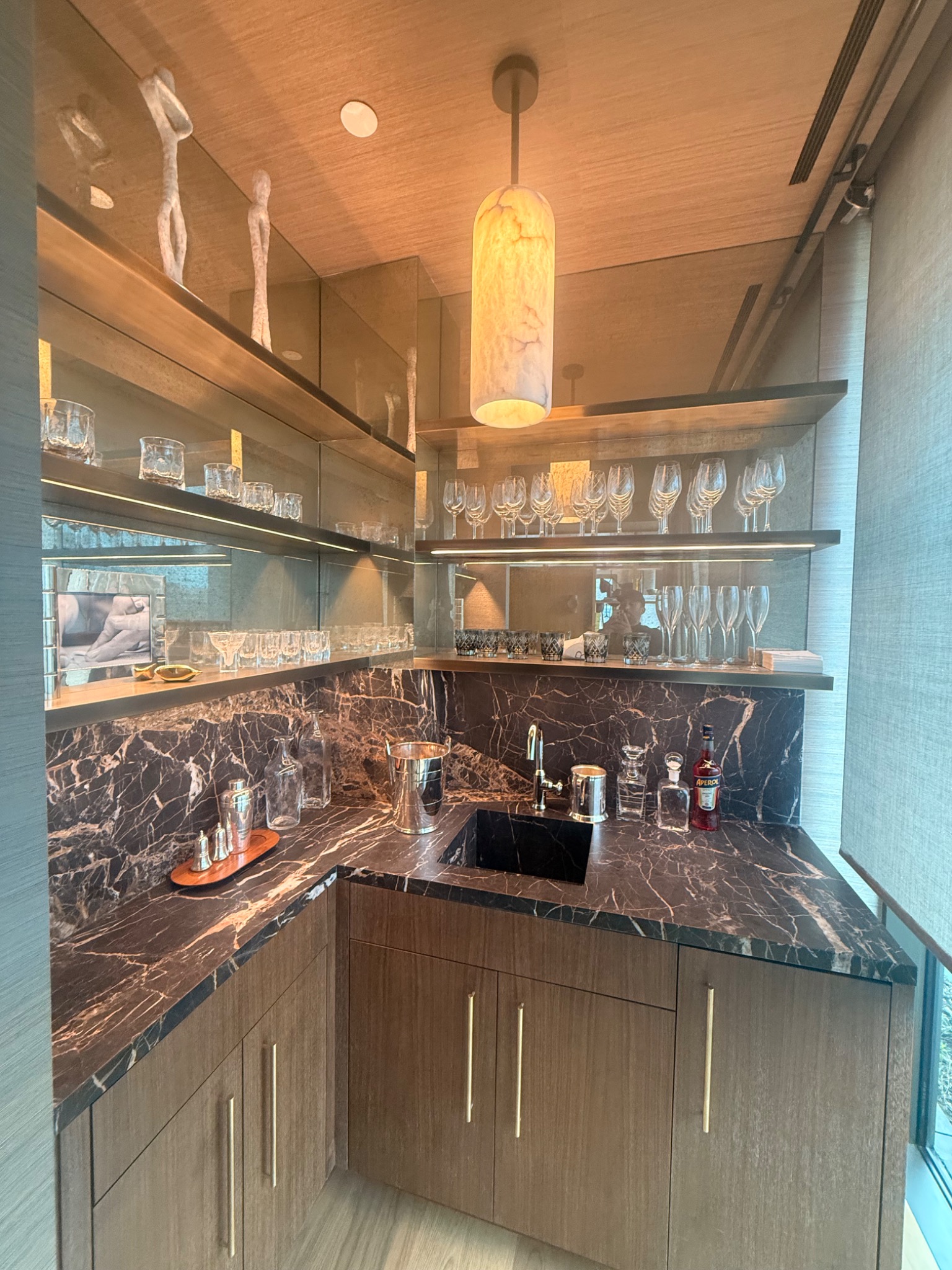 Finished custom bar with cabinetry, marble surfaces, mirrors, and pendant lighting