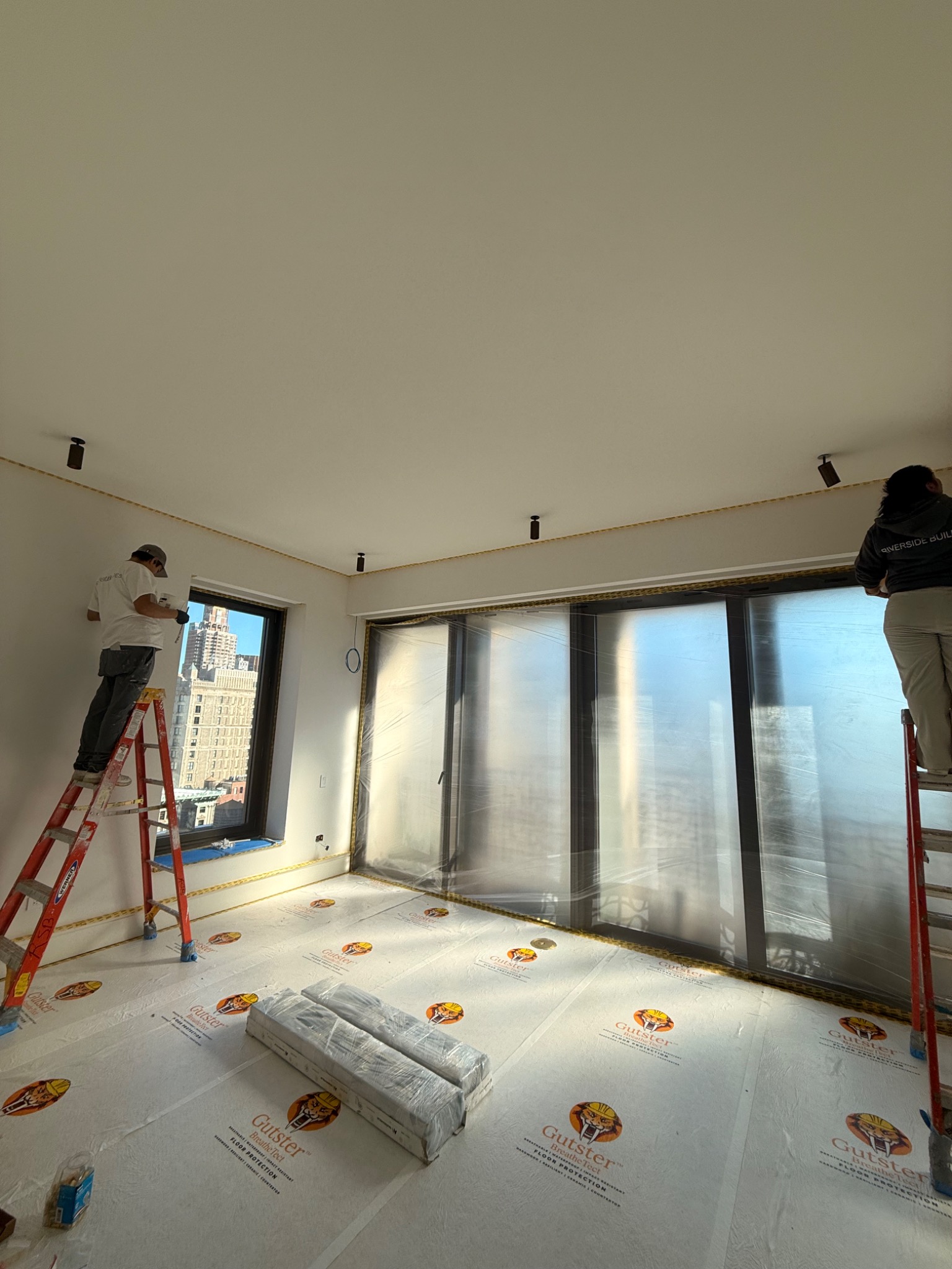 Residential living room under construction with workers installing ceiling lighting